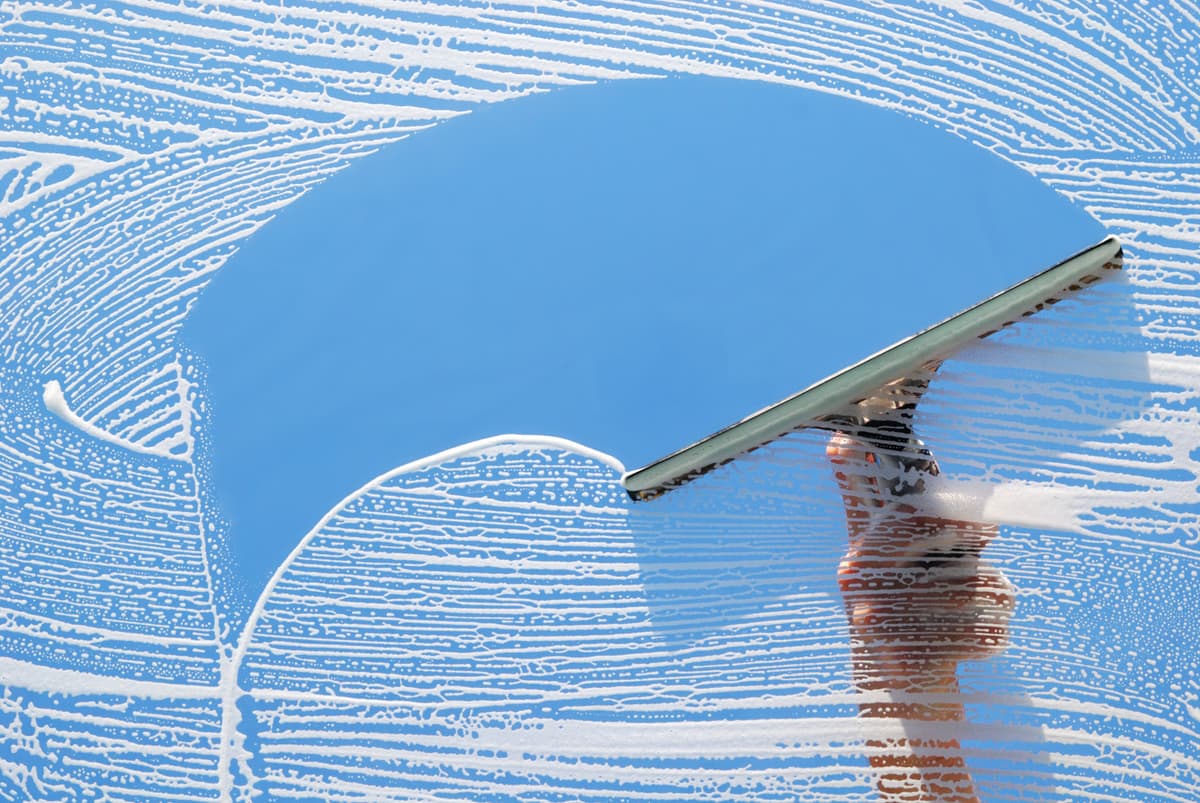 Hands using a squeegee on a soapy window